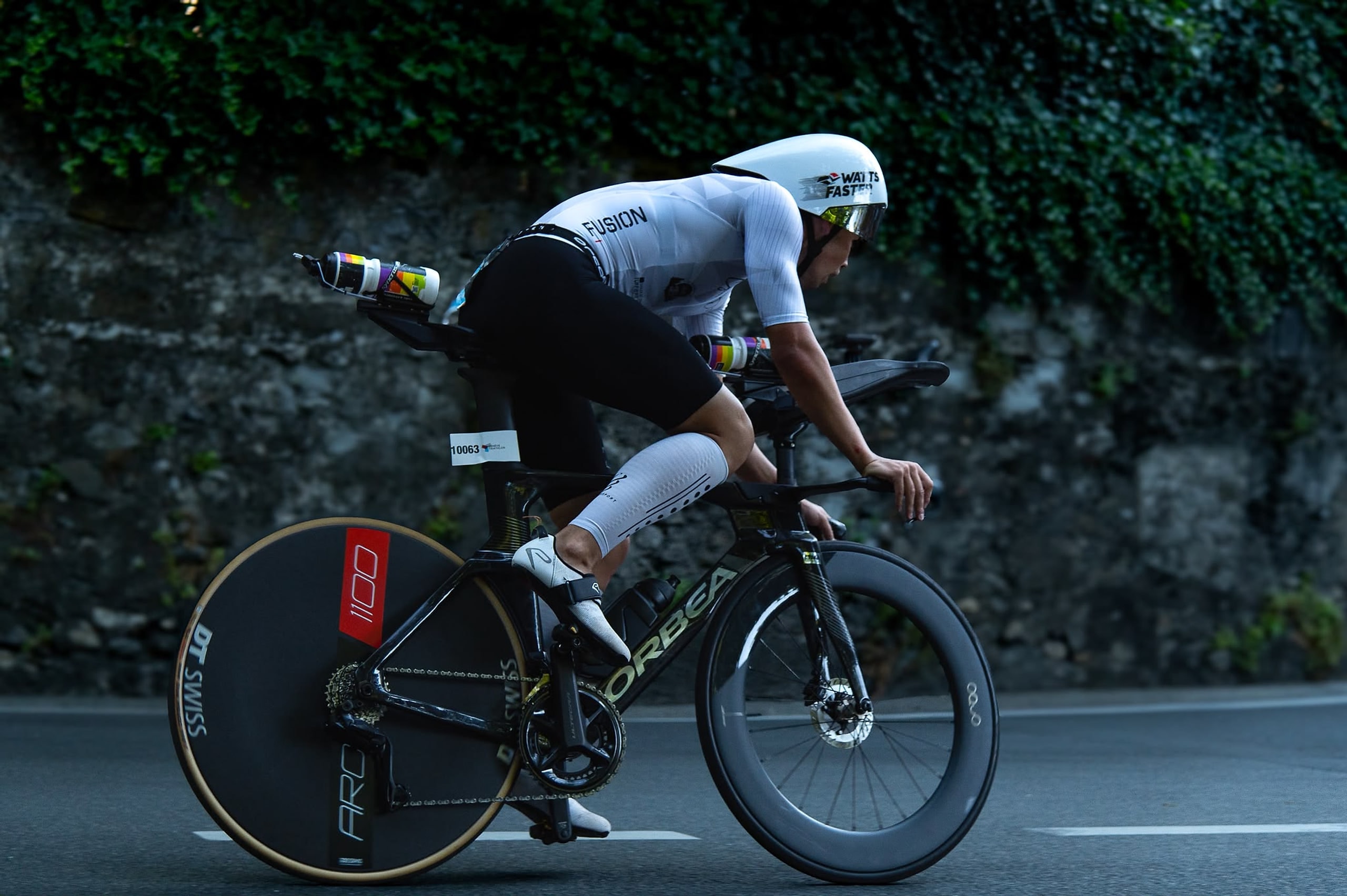 Triathlète en position aérodynamique sur son vélo de contre-la-montre, sur une route bordée d’un mur végétal